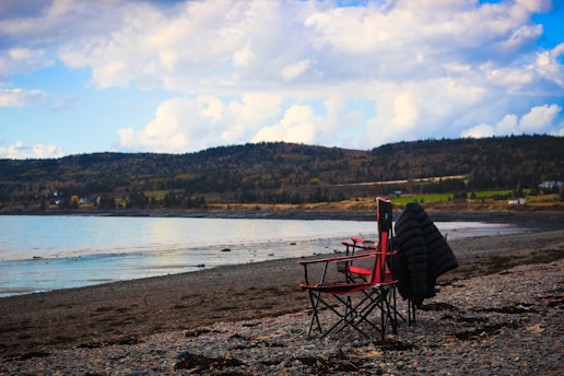 A rugged leather jacket draped over a weathered wooden chair on a rocky coastline at sunset.