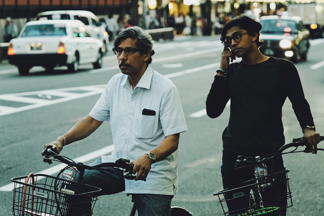 selective focus photography of two man riding bicycle on concrete road during daytime