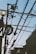 A network of black utility cables stretches across the sky with a streetlight featuring a round bulb and a power pole supporting various electrical equipment. The background includes the outlines of buildings and a clear sky.
