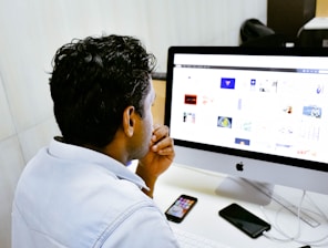 man sitting in front of silver Apple iMac on table