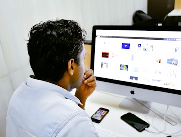 man sitting in front of silver Apple iMac on table