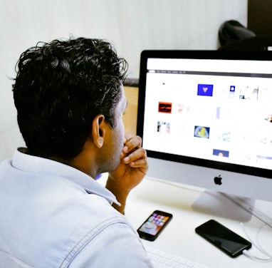 man sitting in front of silver Apple iMac on table