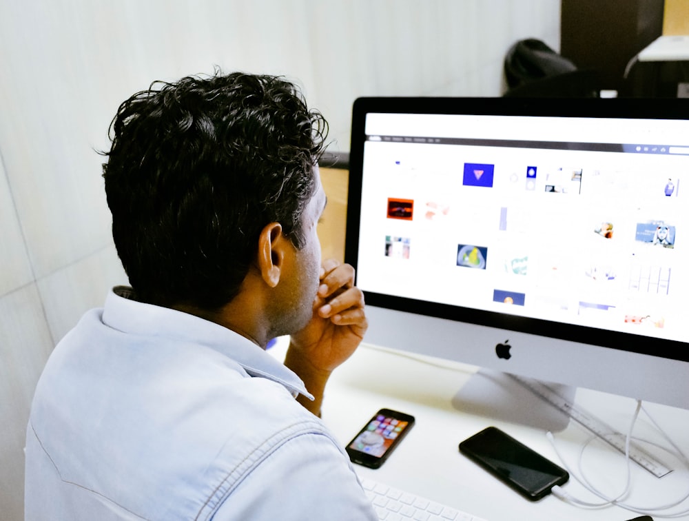 man sitting in front of silver Apple iMac on table