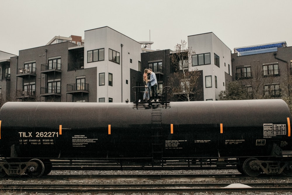 man and woman kissing on train near buildings