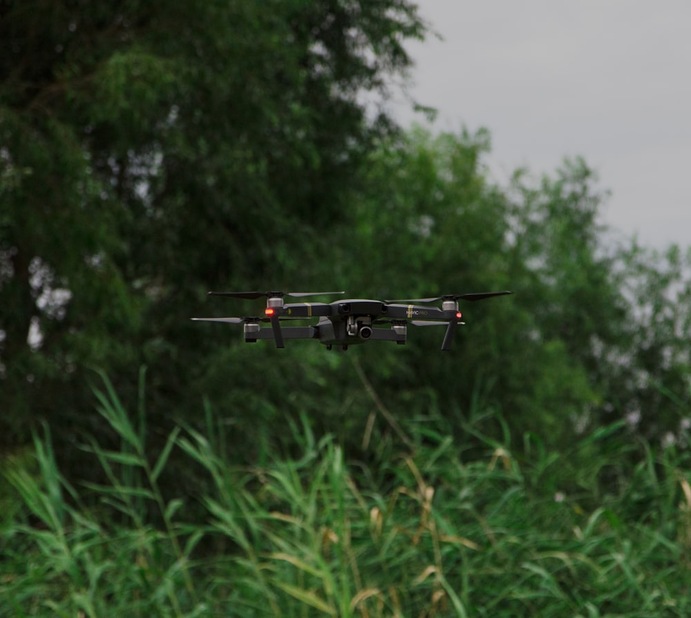 flying black drone front of tree