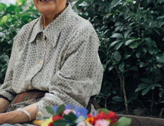 An elderly woman smiling warmly while chatting with a companion during a walk in a garden.