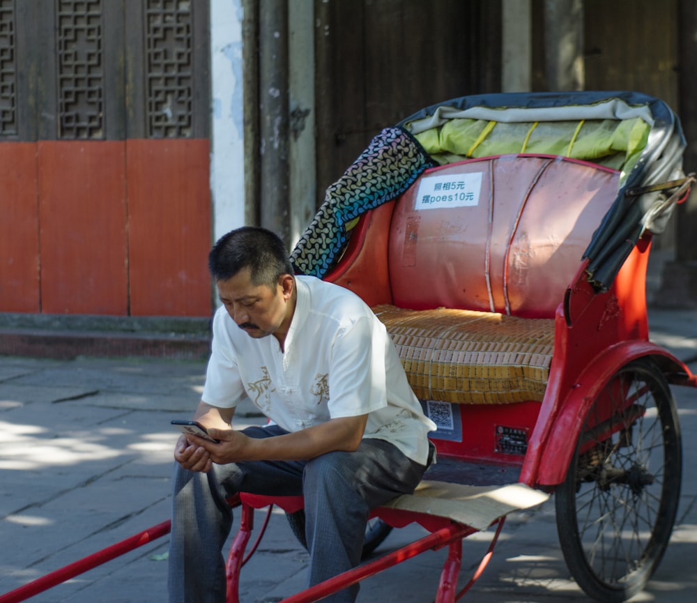 man sitting on red trailer using smartphone