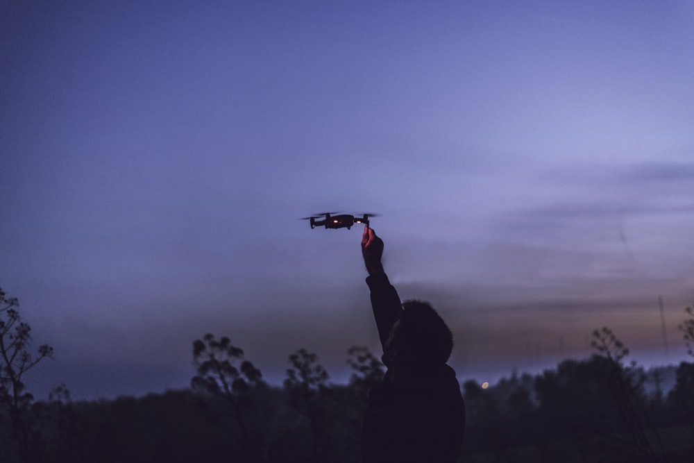 person using black quadcopter drone during nighttime