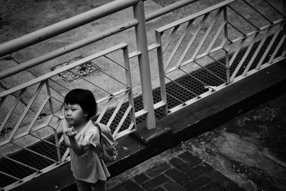 grayscale photography of toddler standing beside rail