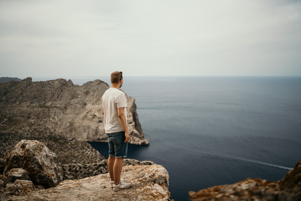 man standing on mountain range near body of water