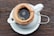 A close-up of a stack of coffee filter papers on a wooden table, with a steaming cup of coffee in the background.