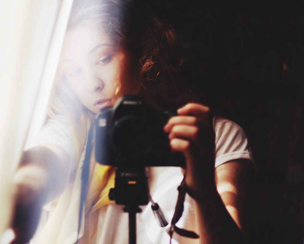 woman holding DSLR camera beside white curtain