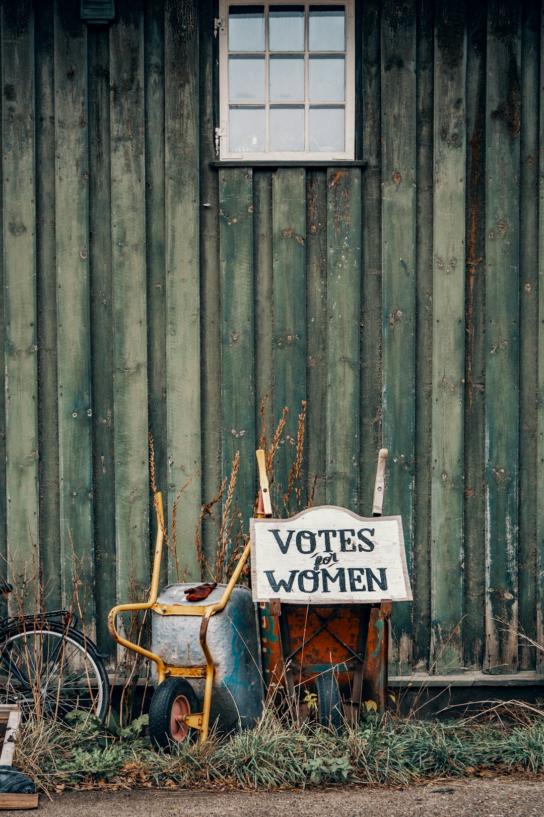 two wheelbarrows with votes for women sign on green wall