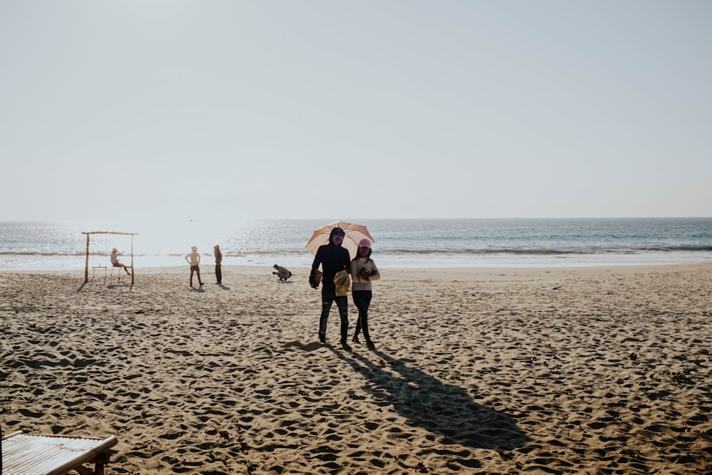 2 person under umbrella at shore during daytime