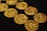 Several intricately detailed gold coins are scattered across a black surface, showcasing their textured surfaces and gleaming metallic shine.