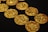Several intricately detailed gold coins are scattered across a black surface, showcasing their textured surfaces and gleaming metallic shine.