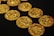 Several intricately detailed gold coins are scattered across a black surface, showcasing their textured surfaces and gleaming metallic shine.