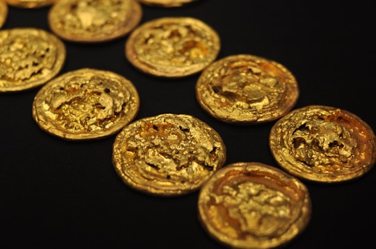 Several intricately detailed gold coins are scattered across a black surface, showcasing their textured surfaces and gleaming metallic shine.