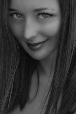 A close-up black and white portrait of a young woman with long hair. She has a gentle smile and bright eyes, with her face slightly angled to one side. The lighting highlights the softness of her features.