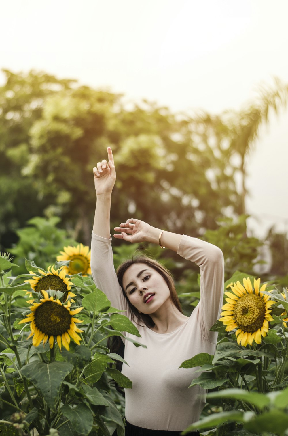 mujer levantando la mano rodeada de girasoles durante el día