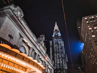 An urban nightscape featuring art deco architecture illuminated by warm streetlights.