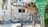 A vibrant, eclectic courtyard filled with colorful mosaic art. The walls are adorned with intricate patterns, sculptures, and various artistic elements including tiles and murals. A large, decorative metal structure and a green column with artistic designs are also present.