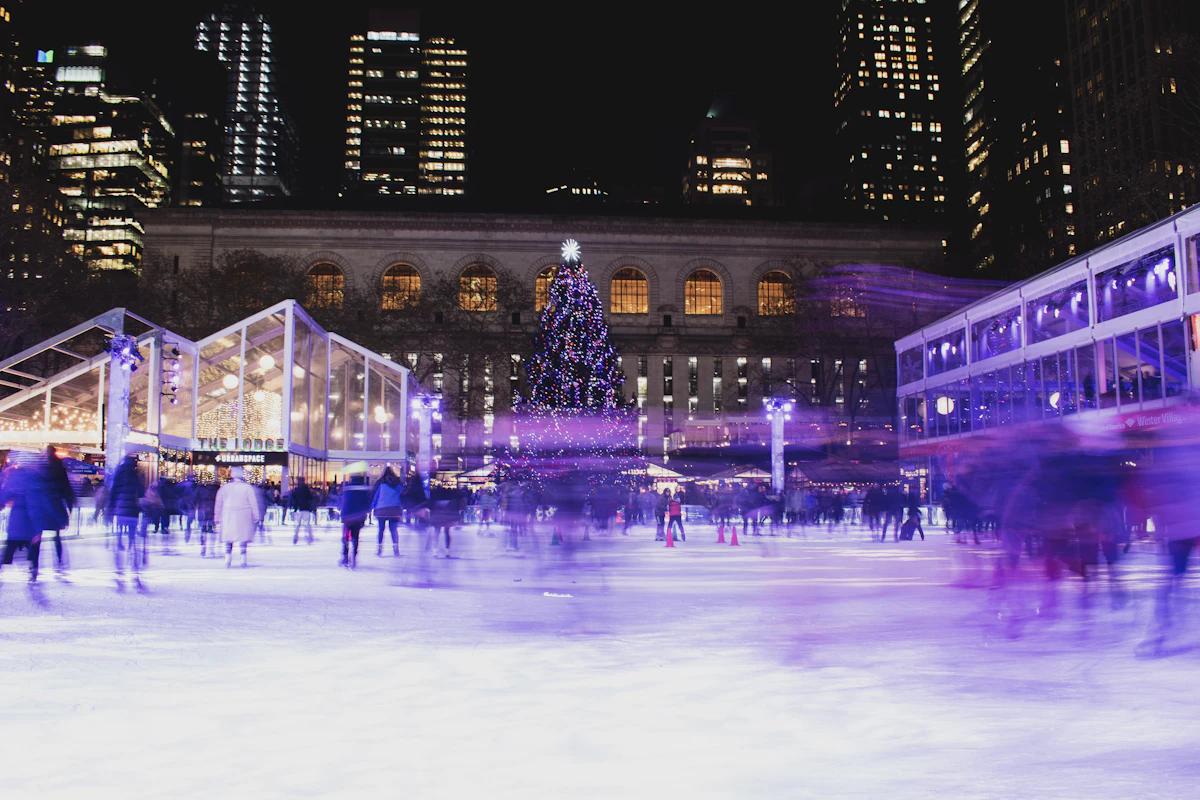 Crowd skating on the ice rink at Bryant Park at night with lit market stalls around it