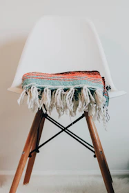 Modern footrest placed beside a reading chair with a colorful throw blanket.