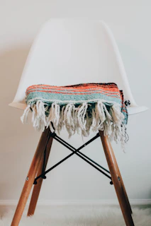 Modern footrest placed beside a reading chair with a colorful throw blanket.