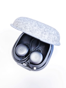 A pair of black earphones rests inside an open gray fabric case. The earphones have a circular design with a cord looped around them.