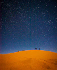 Group of travelers sharing a sunset moment in the Sahara desert camp under starry sky.