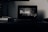 A dark room with a laptop open on a desk. The laptop screen displays a black and white scene from the film 'ROMA', with text about its duration and director. Beside the laptop, there are two closed notebooks and a pen.