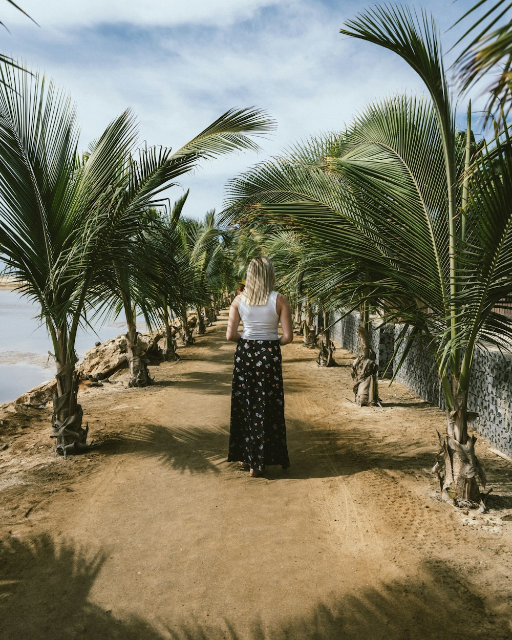 woman in maxi skirt stands in the middle of dirt road with palm trees