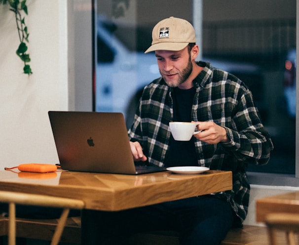 man sitting while having coffee and using laptop