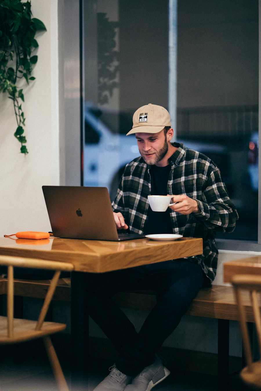 Ein Mann arbeitet mit einem Laptop und einer Tasse Kaffee an einem Holztisch im Café