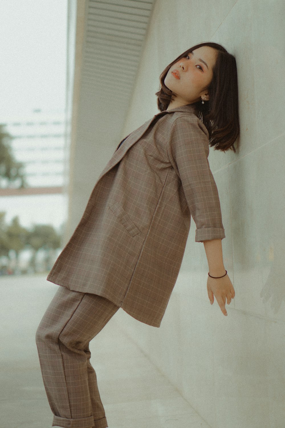 femme portant un blazer et un pantalon marron appuyée sur le mur