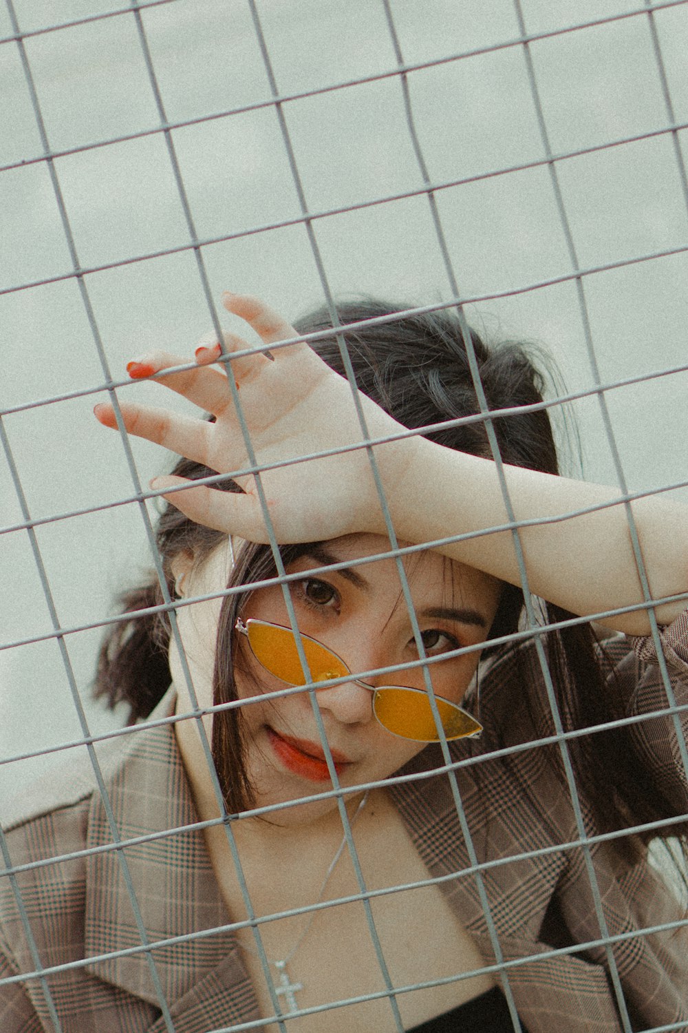 woman wearing brown blazer and sunglasses leaning on chain link fence