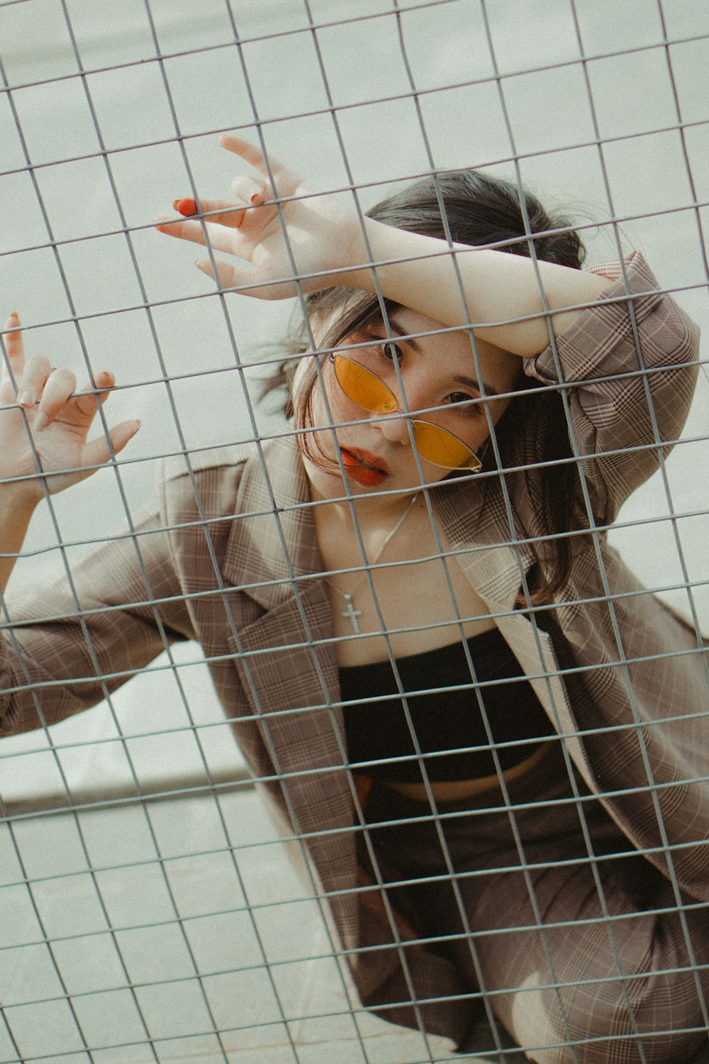 woman in brown suit leaning on gray cyclone fence