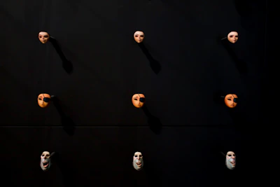 A shadowy display of several eerie masks hanging against a muted rust backdrop.