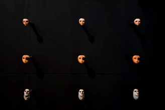 A shadowy display of several eerie masks hanging against a muted rust backdrop.