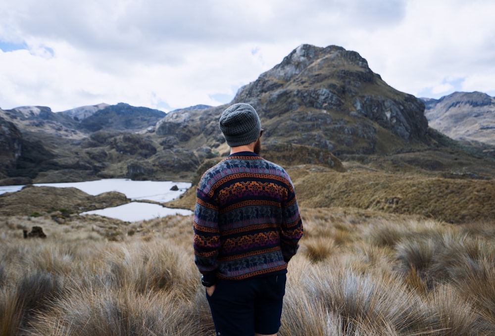 man in sweater and bermuda shorts stands in grass covered ground