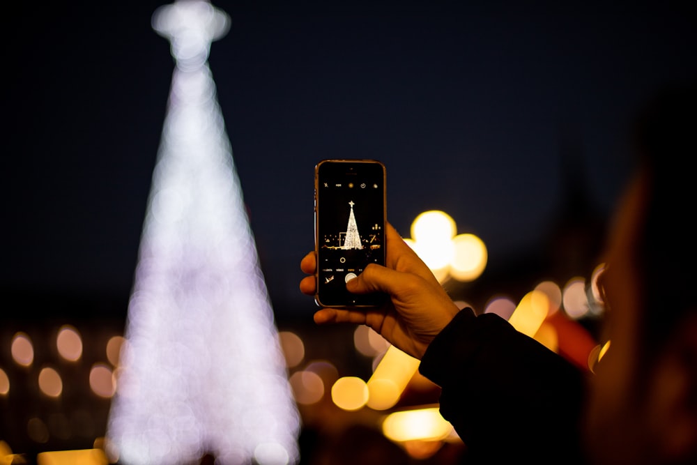 person holding smartphone taking photo of christmas tree