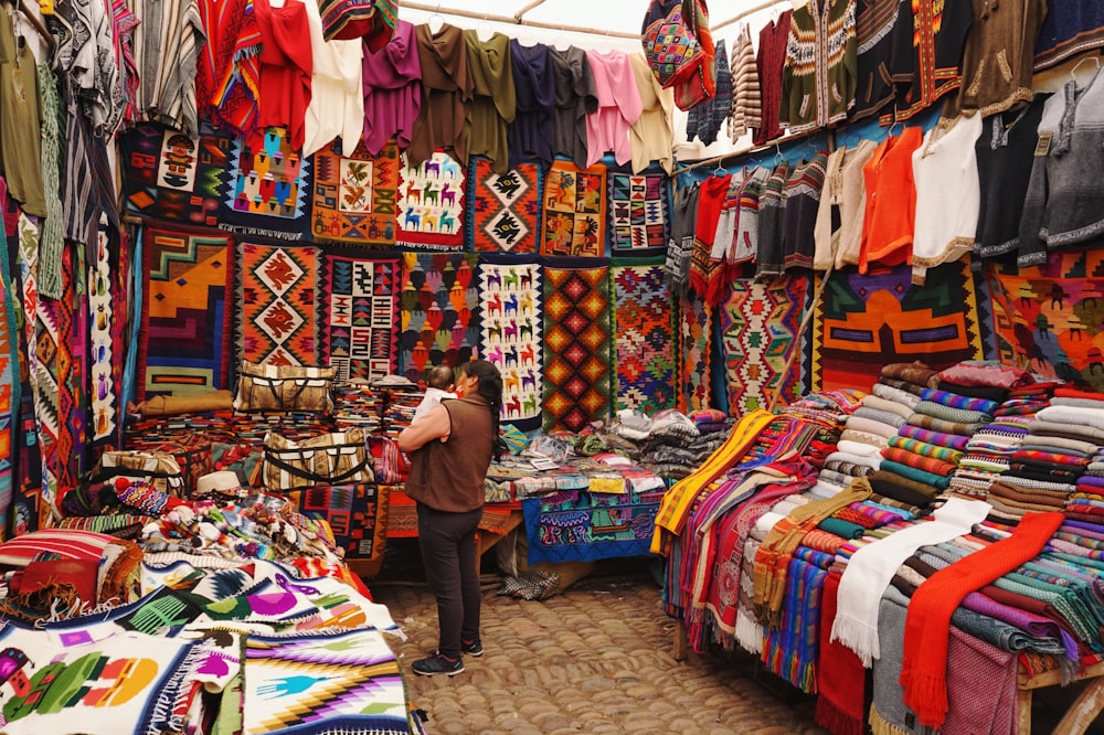 Frau im Geschäft mit Auslage von verschiedenen Hemden und Textilien