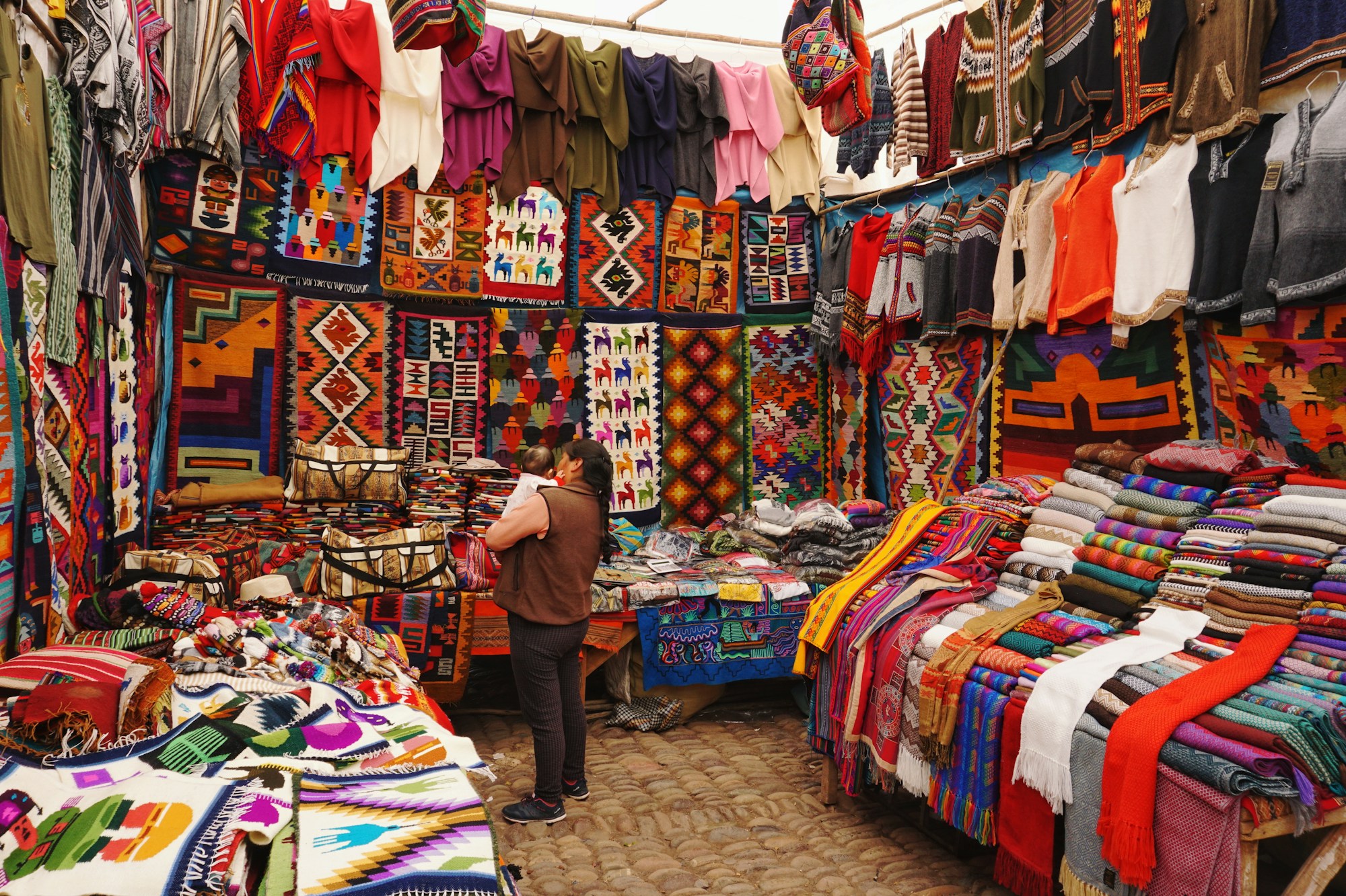 Handwoven Andean textiles and alpaca sweaters at a market stall in the Cusco region of Peru