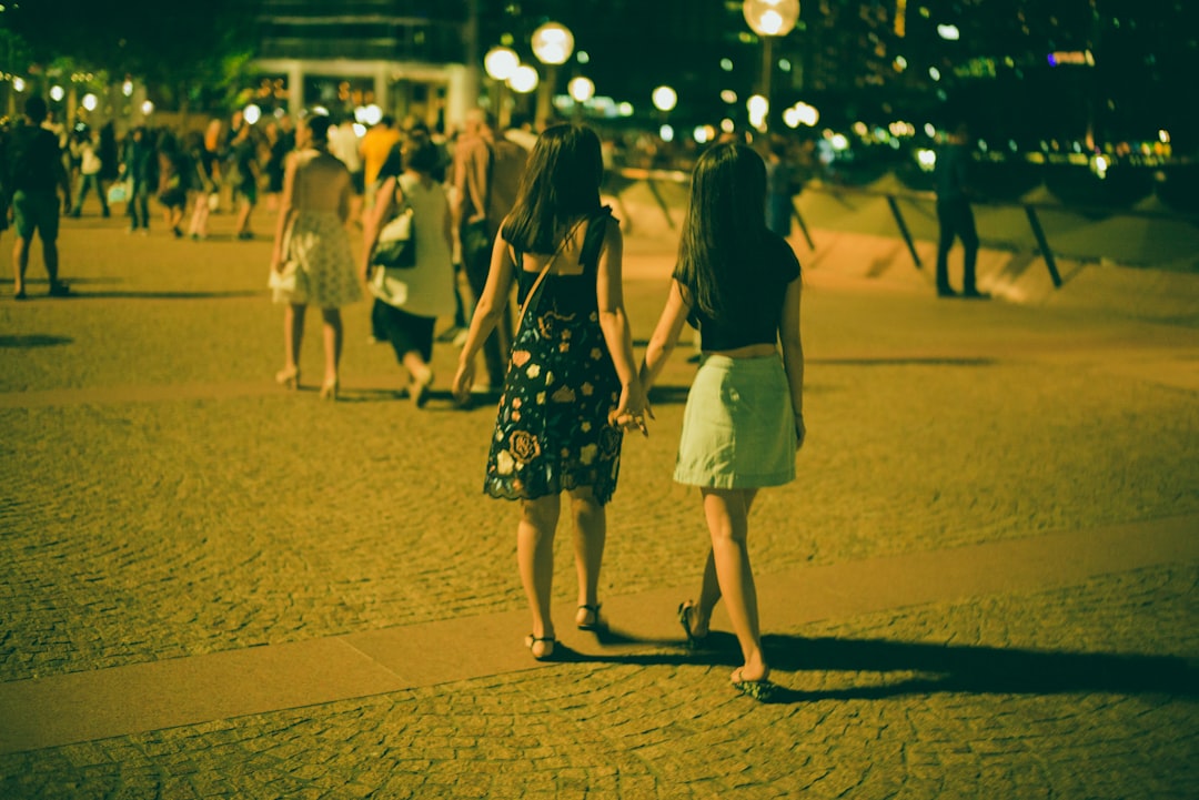two girl holding hands walking on road at nighttime