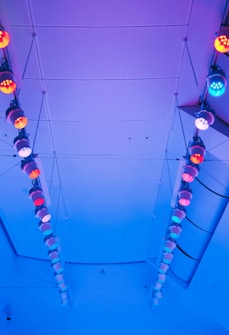A ceiling with rows of colored spotlights casting hues of blue, red, and orange. The lights are aligned symmetrically, mounted on tracks, creating a modern and artistic ambiance.