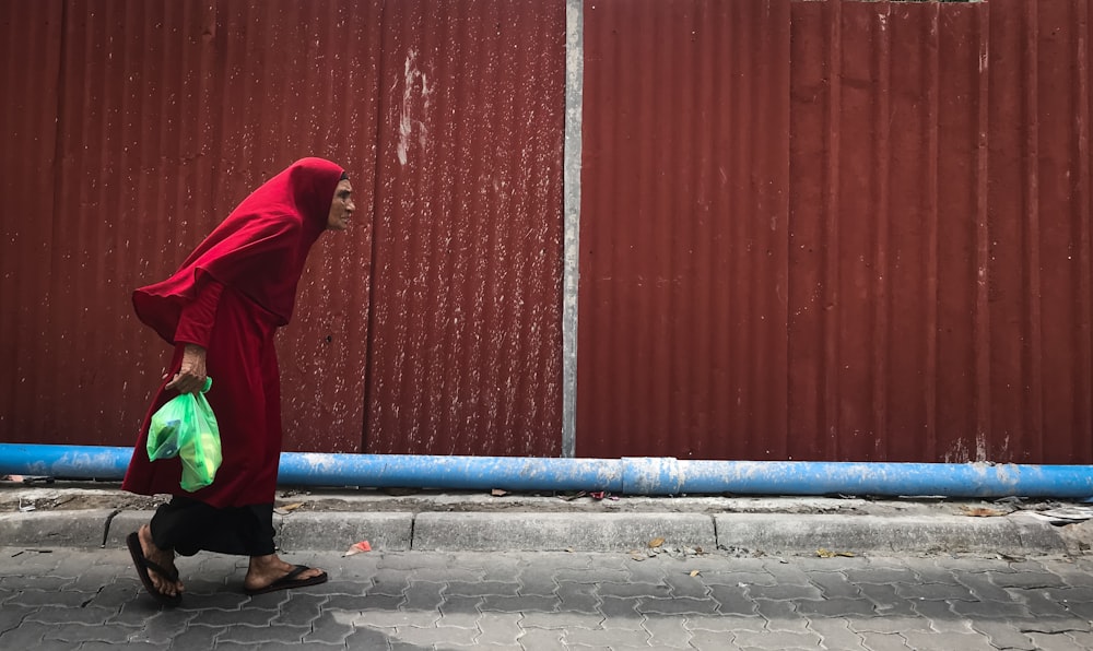 person walking near red metal wall during daytime