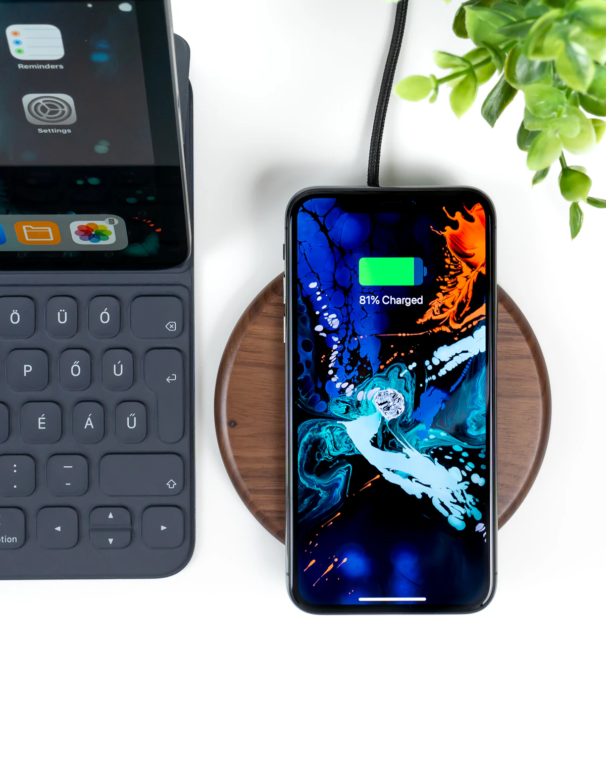 Smartphone charging on a wooden wireless charging dock beside a keyboard