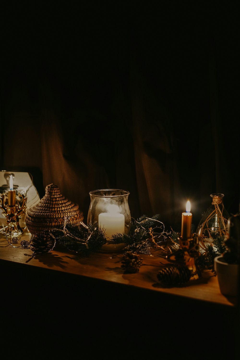 lighted candle near jars and pine cone on table