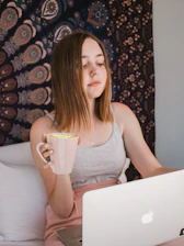 A young Indian woman working comfortably on her laptop at home with a cup of tea nearby.